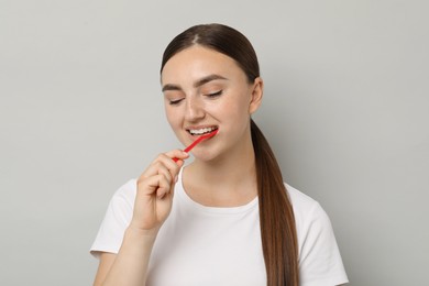 Beautiful woman brushing her teeth on gray background