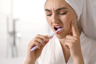 Young woman suffering from toothache while brushing her teeth in bathroom