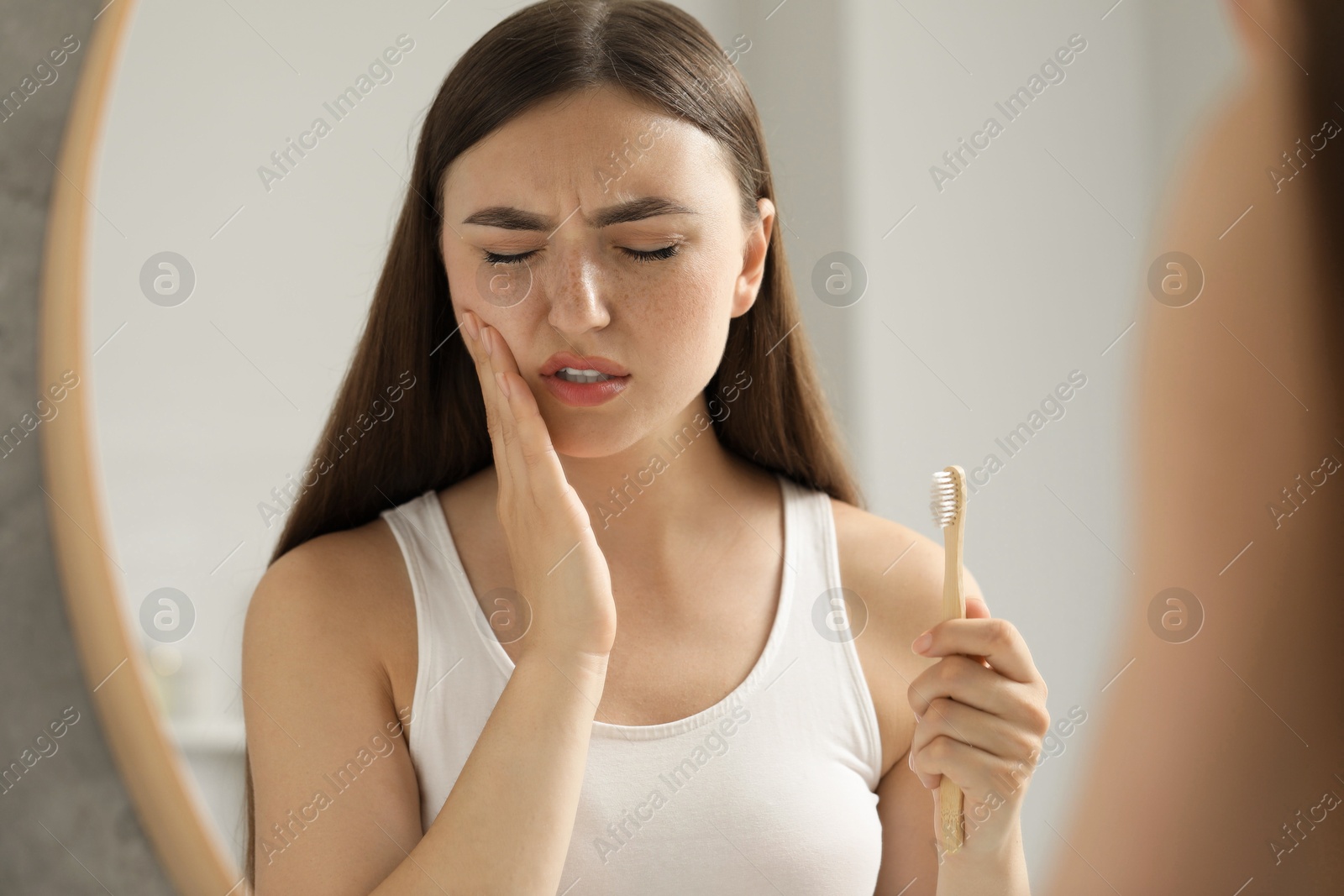 Photo of Young woman with toothbrush suffering from toothache in bathroom