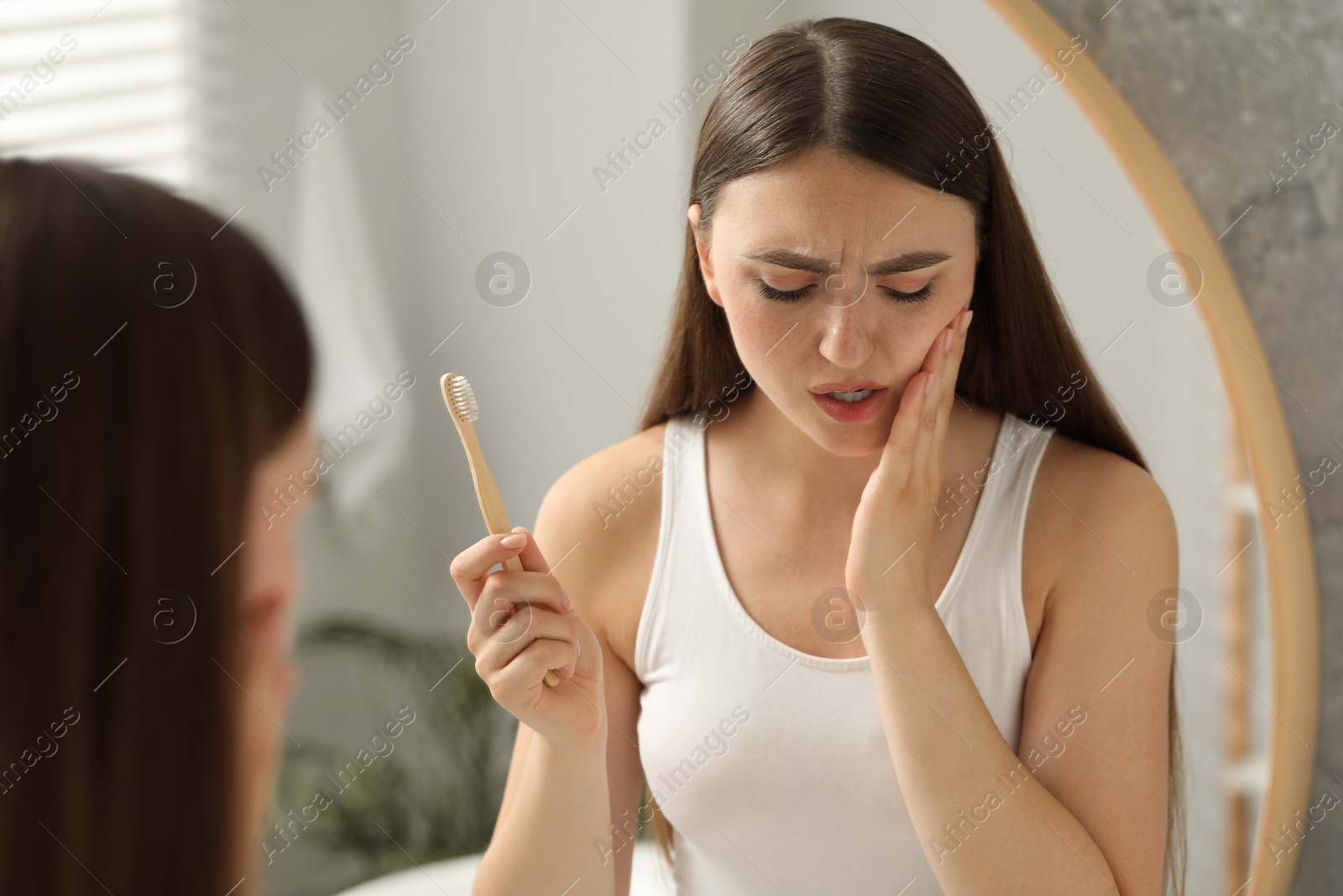 Photo of Young woman with toothbrush suffering from toothache in bathroom