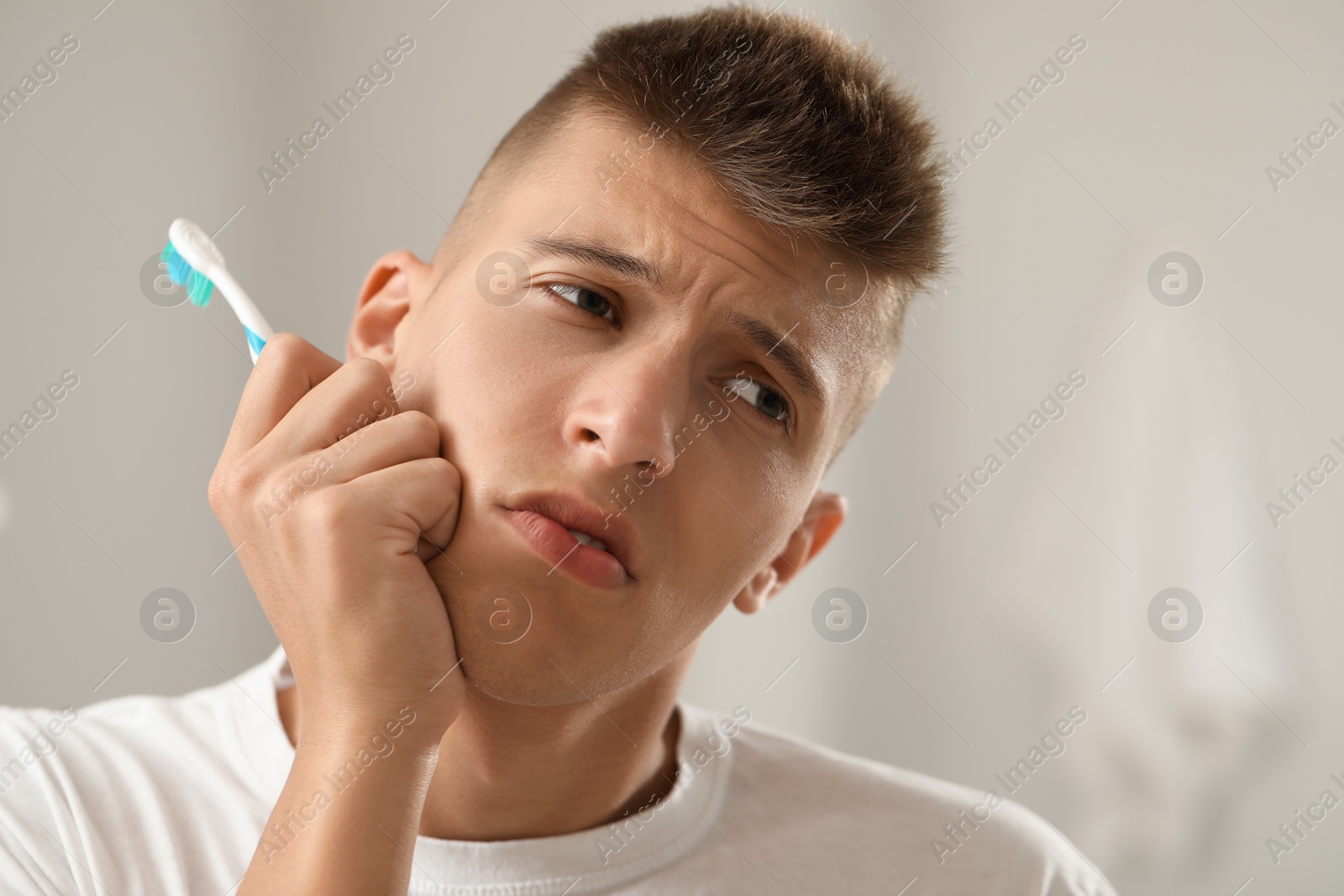 Photo of Young man with toothbrush suffering from toothache in bathroom