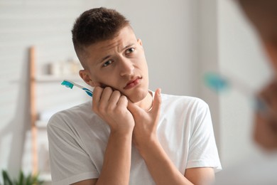 Young man with toothbrush suffering from toothache in bathroom