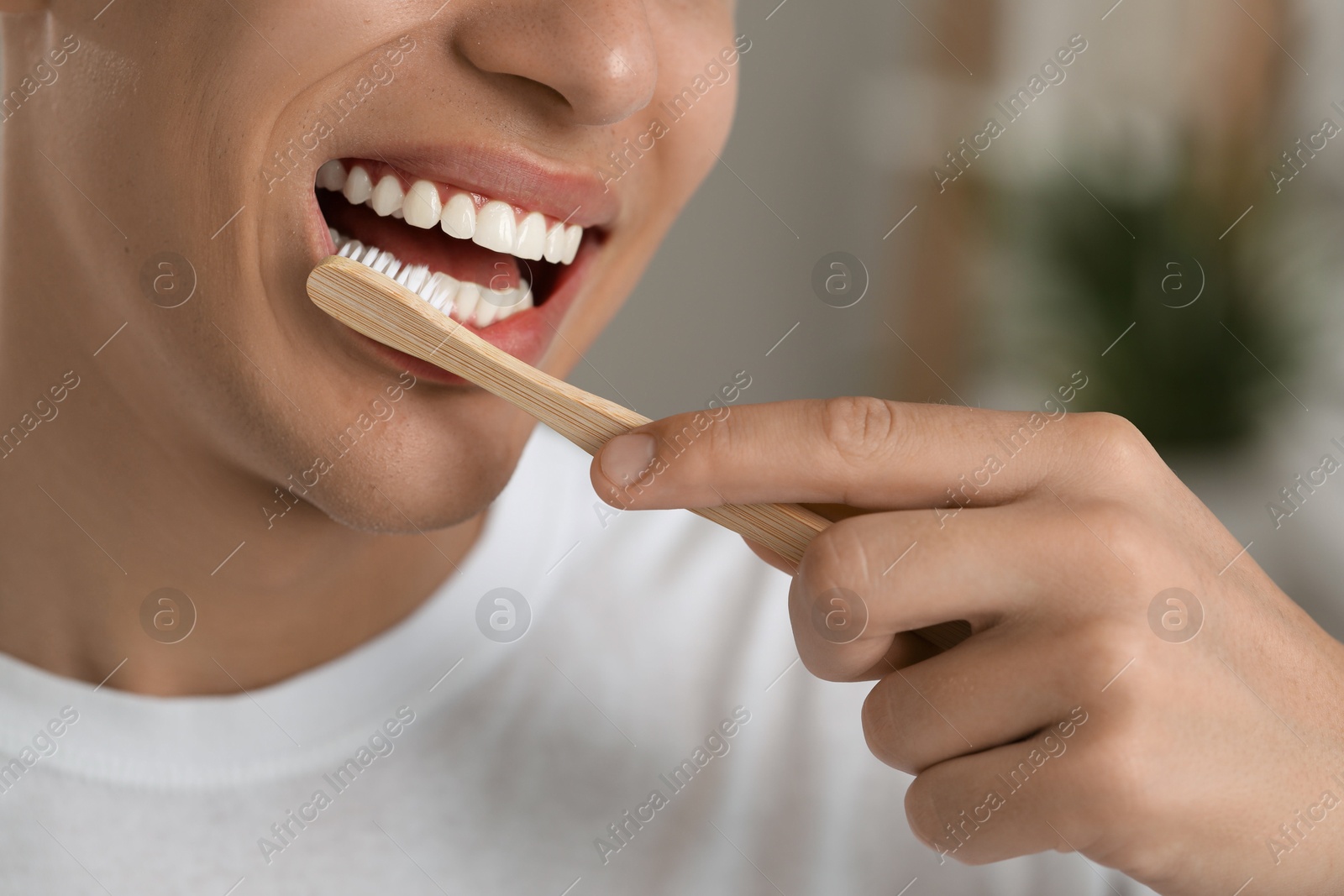 Photo of Young man brushing his teeth in bathroom, closeup