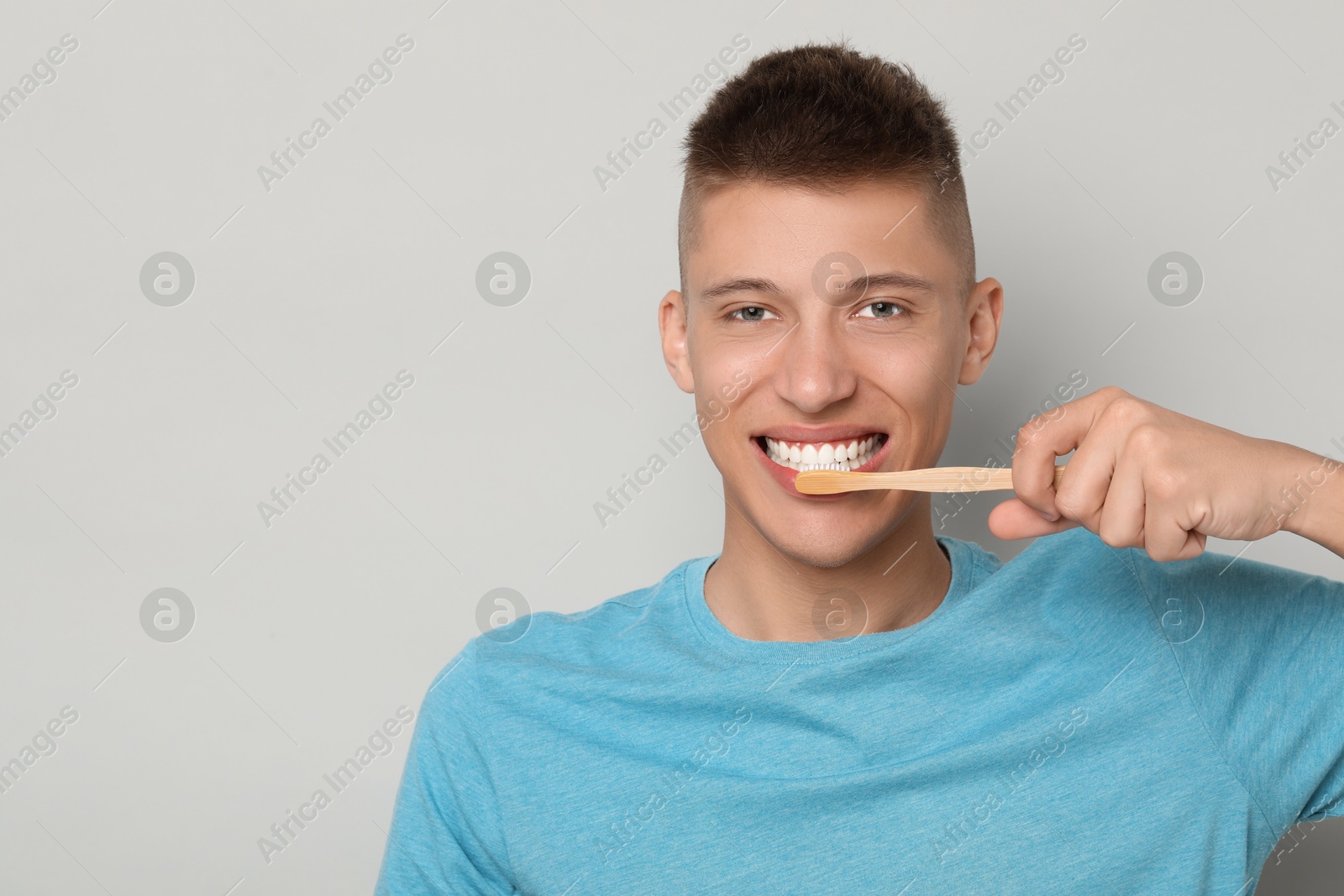 Photo of Young man brushing his teeth on gray background, space for text