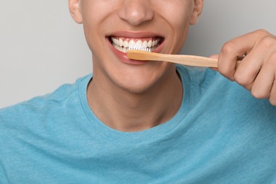 Photo of Young man brushing his teeth on gray background, closeup