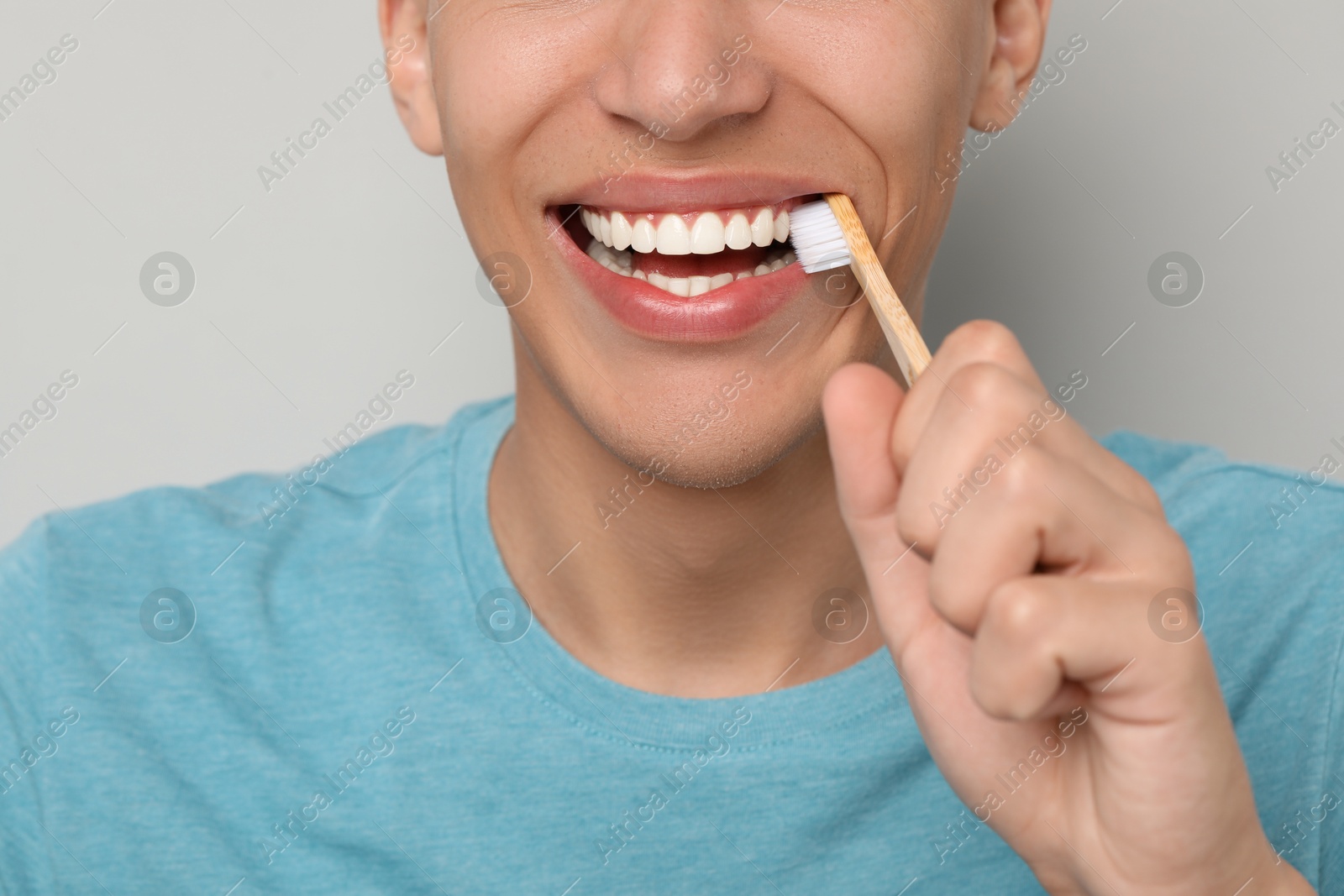 Photo of Young man brushing his teeth on gray background, closeup