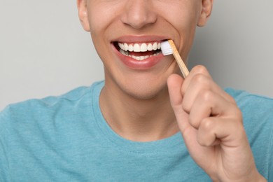 Photo of Young man brushing his teeth on gray background, closeup