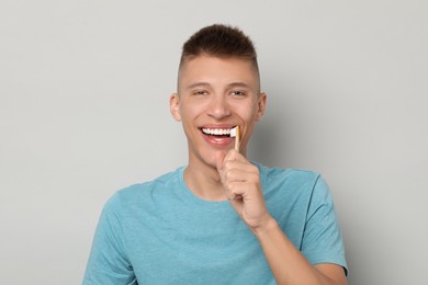 Young man brushing his teeth on gray background