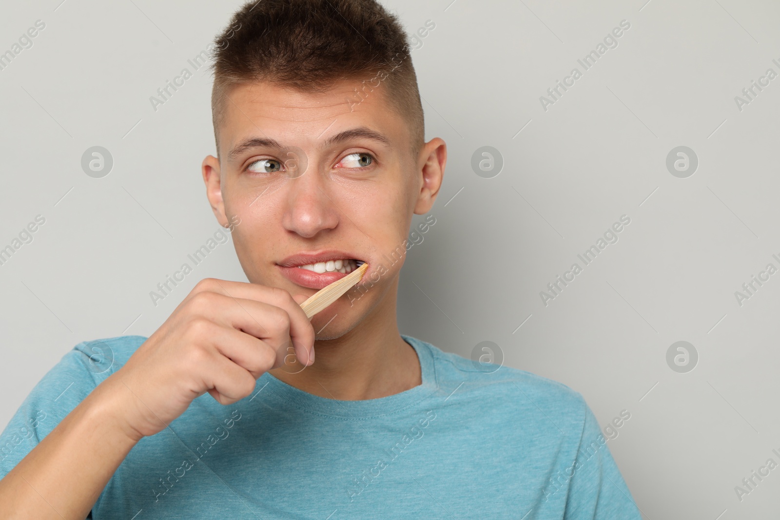 Photo of Young man brushing his teeth on gray background, space for text