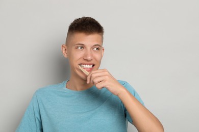 Photo of Young man brushing his teeth on gray background