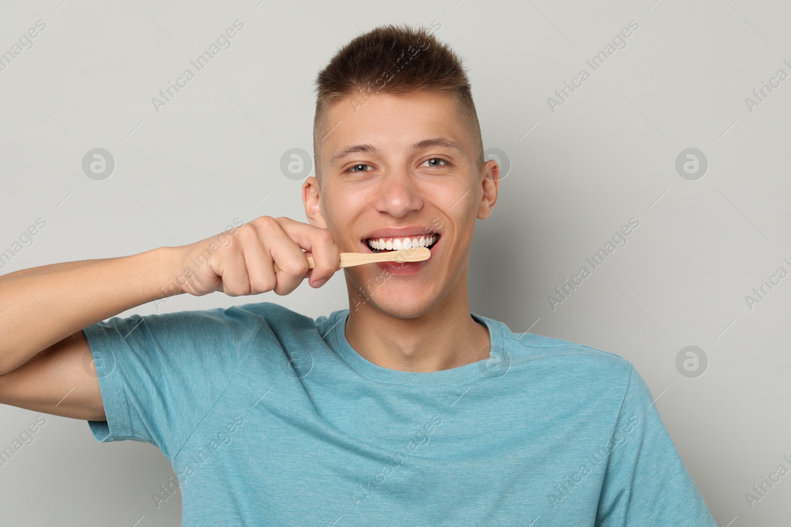 Photo of Young man brushing his teeth on gray background