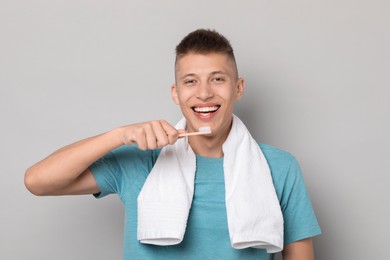 Young man brushing his teeth on gray background