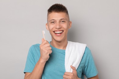 Happy young man with toothbrush on gray background