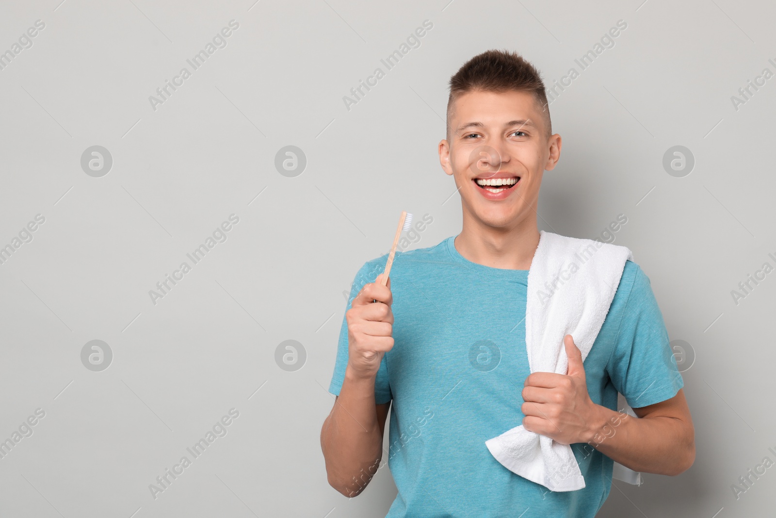 Photo of Happy young man with toothbrush on gray background, space for text