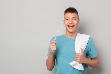 Happy young man with toothbrush on gray background, space for text