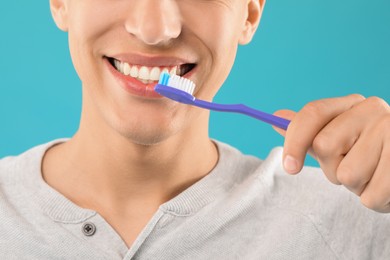 Photo of Young man brushing his teeth on light blue background, closeup