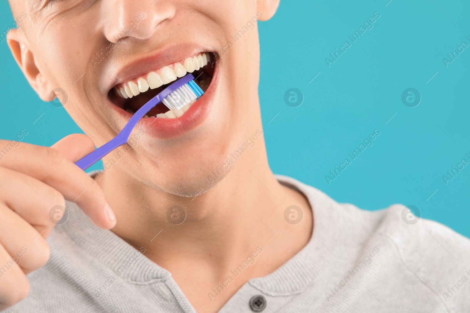 Photo of Young man brushing his teeth on light blue background, closeup