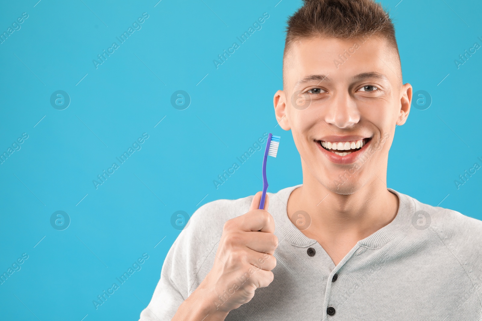 Photo of Happy young man with toothbrush on light blue background, space for text