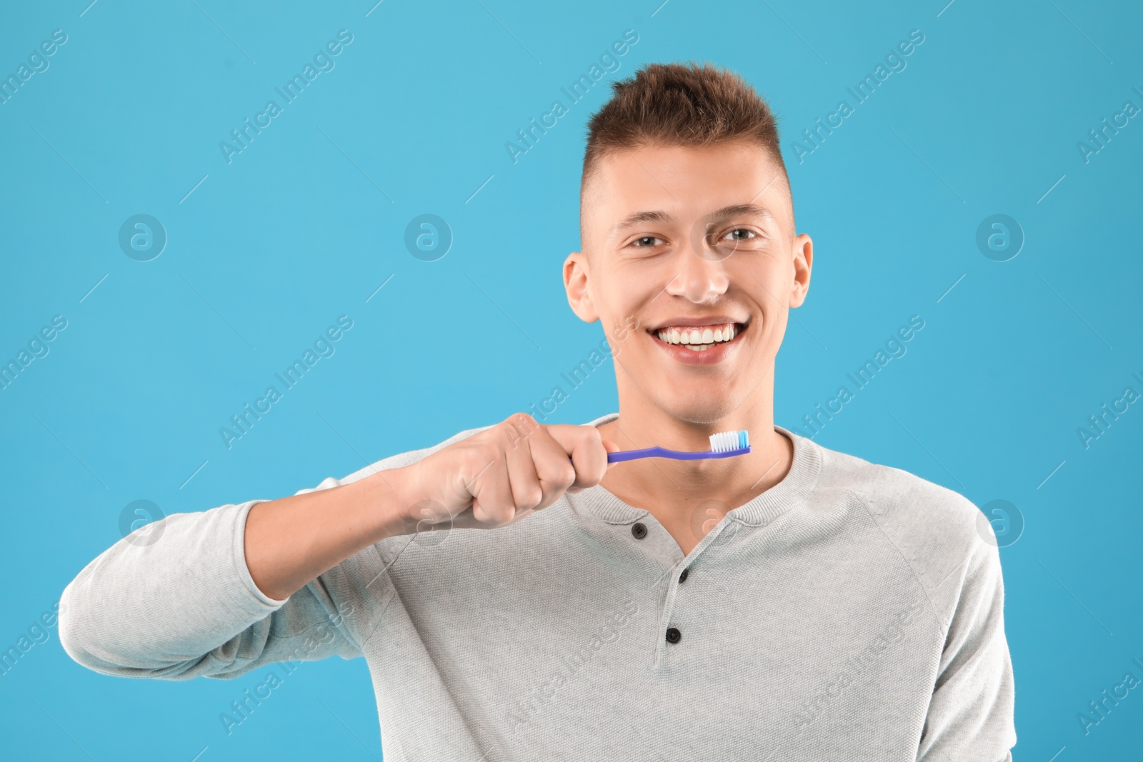 Photo of Happy young man with toothbrush on light blue background