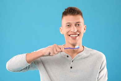 Happy young man with toothbrush on light blue background