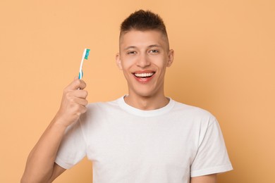 Photo of Happy young man with toothbrush on beige background