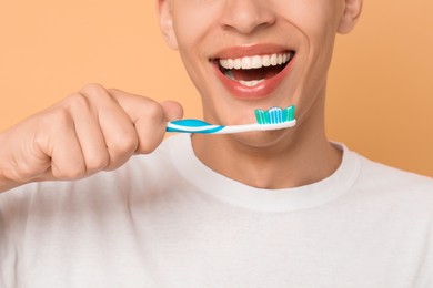 Young man brushing his teeth on beige background, closeup