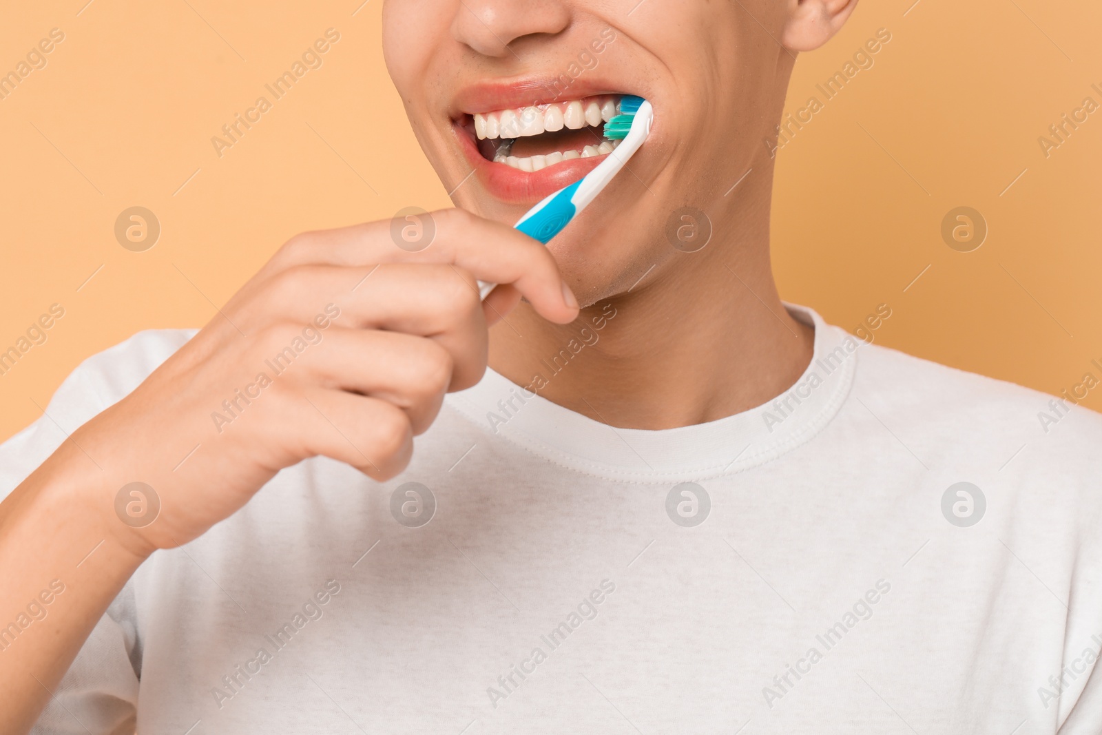 Photo of Young man brushing his teeth on beige background, closeup