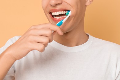 Young man brushing his teeth on beige background, closeup