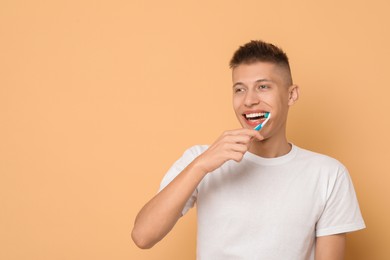 Young man brushing his teeth on beige background, space for text