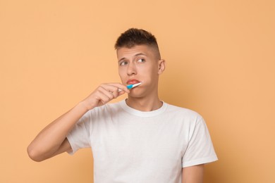 Photo of Young man brushing his teeth on beige background