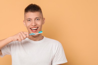 Photo of Young man brushing his teeth on beige background, space for text