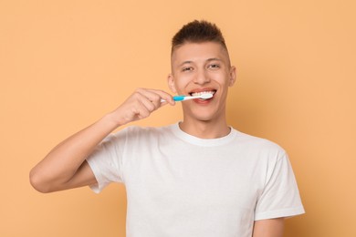 Young man brushing his teeth on beige background