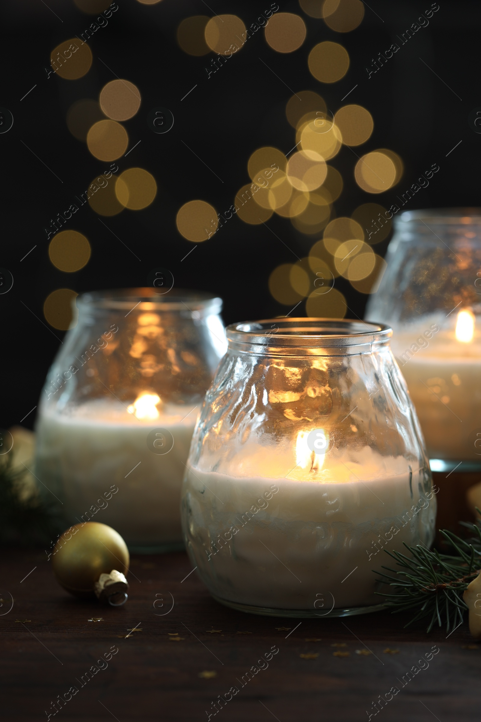 Photo of Burning candles, baubles and fir tree branches on wooden table, closeup