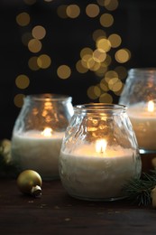 Photo of Burning candles, baubles and fir tree branches on wooden table, closeup