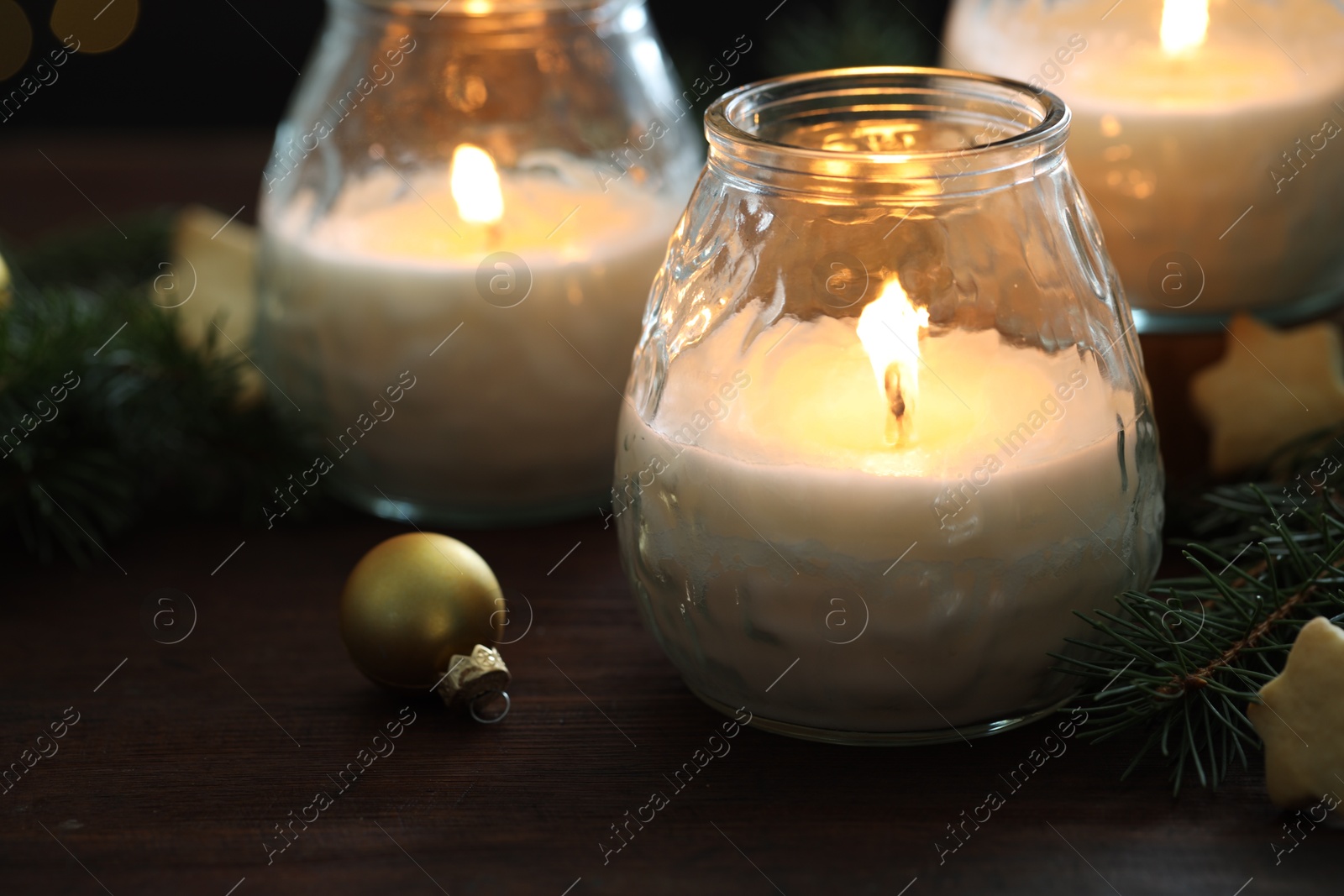 Photo of Burning candles, baubles and fir tree branches on wooden table, closeup