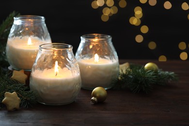 Photo of Burning candles, baubles and fir tree branches on wooden table, closeup