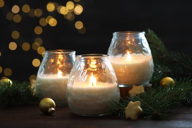 Photo of Burning candles, baubles and fir tree branches on wooden table, closeup