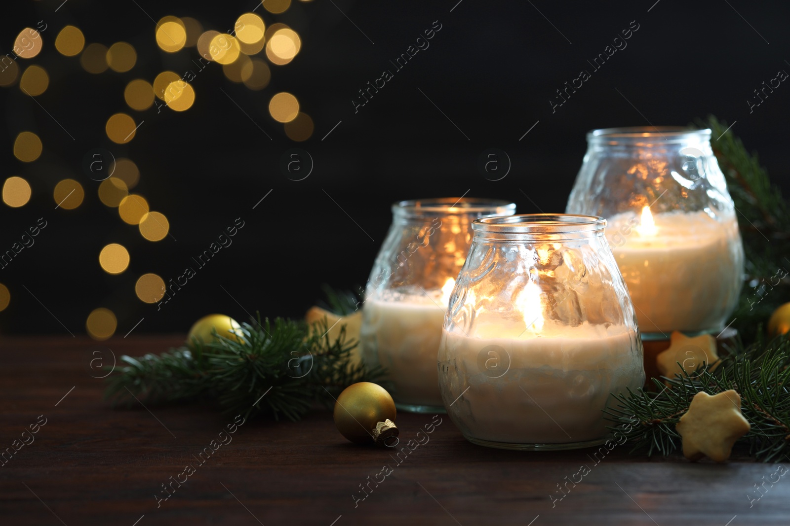 Photo of Burning candles, baubles and fir tree branches on wooden table, closeup. Space for text