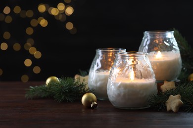 Photo of Burning candles, baubles and fir tree branches on wooden table, closeup. Space for text