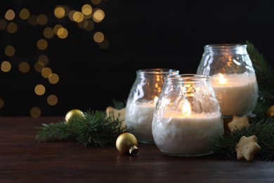 Photo of Burning candles, baubles and fir tree branches on wooden table, closeup. Space for text