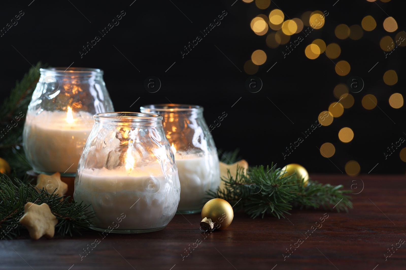 Photo of Burning candles, baubles and fir tree branches on wooden table, closeup. Space for text