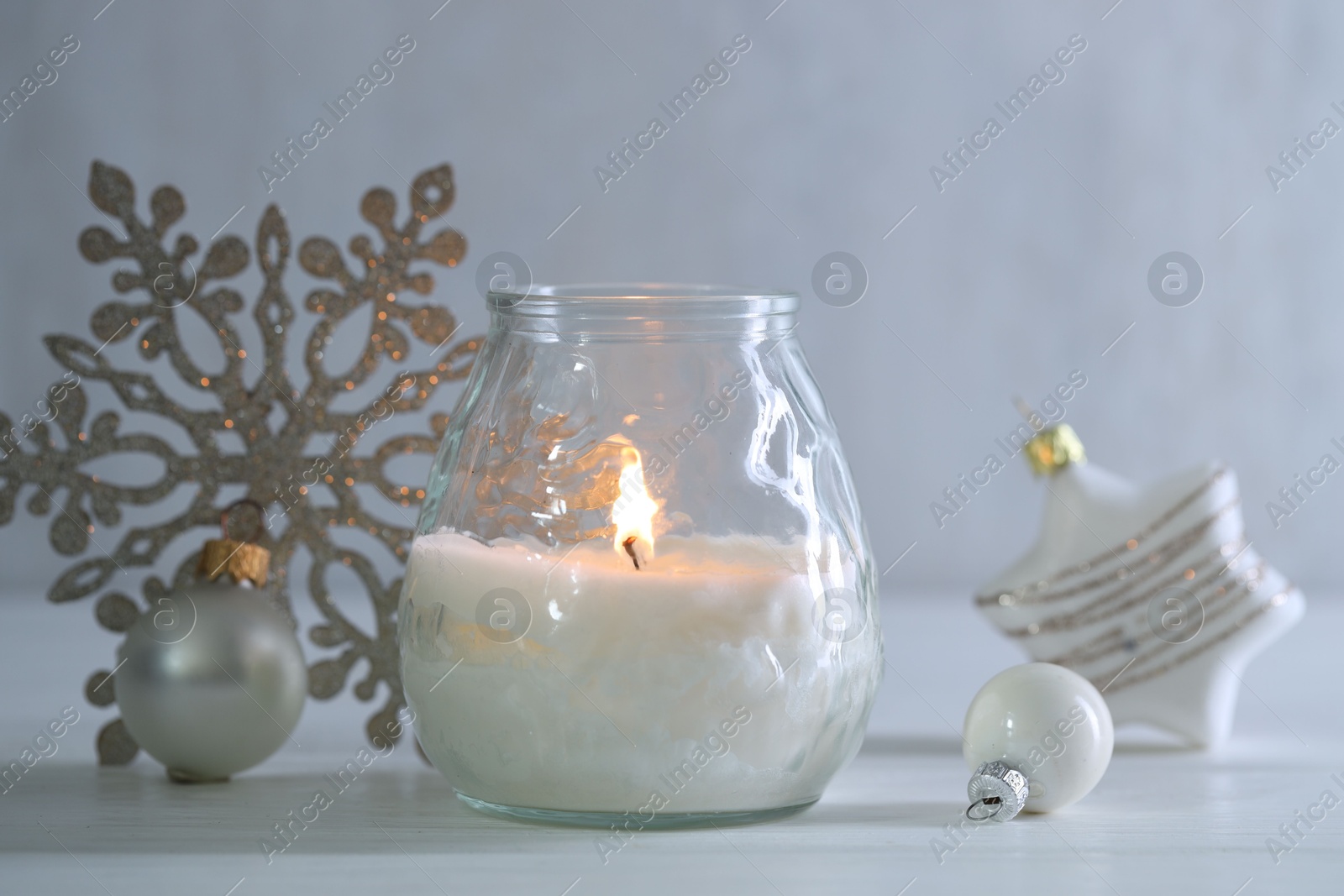 Photo of Burning candle and baubles on white wooden table, closeup