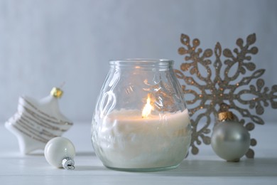 Photo of Burning candle and baubles on white wooden table, closeup