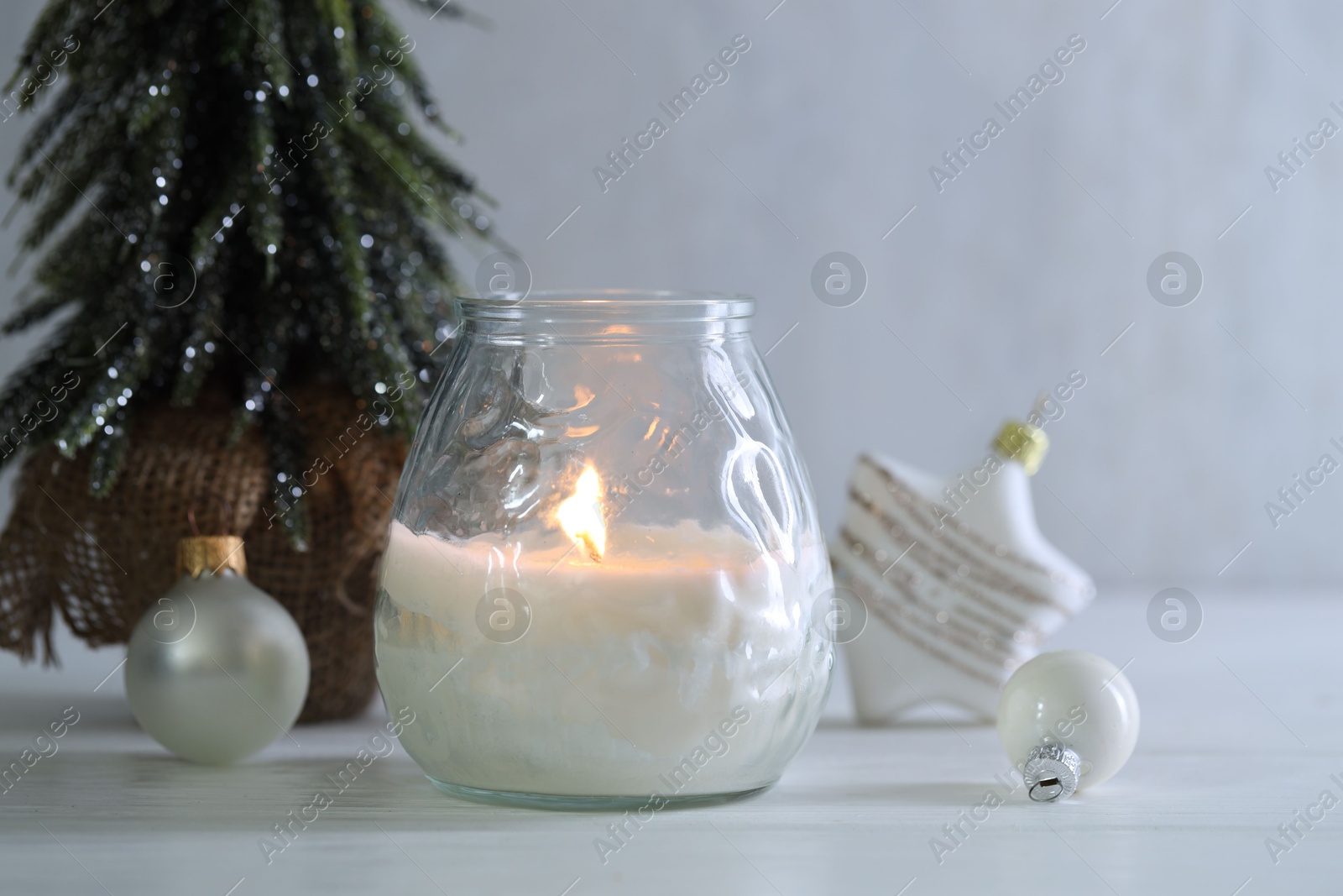 Photo of Burning candle and Christmas decor on white wooden table, closeup