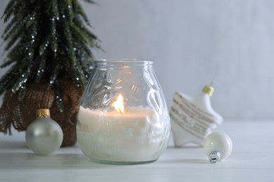 Photo of Burning candle and Christmas decor on white wooden table, closeup