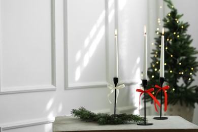 Photo of Burning candles on white table and Christmas tree at home, space for text