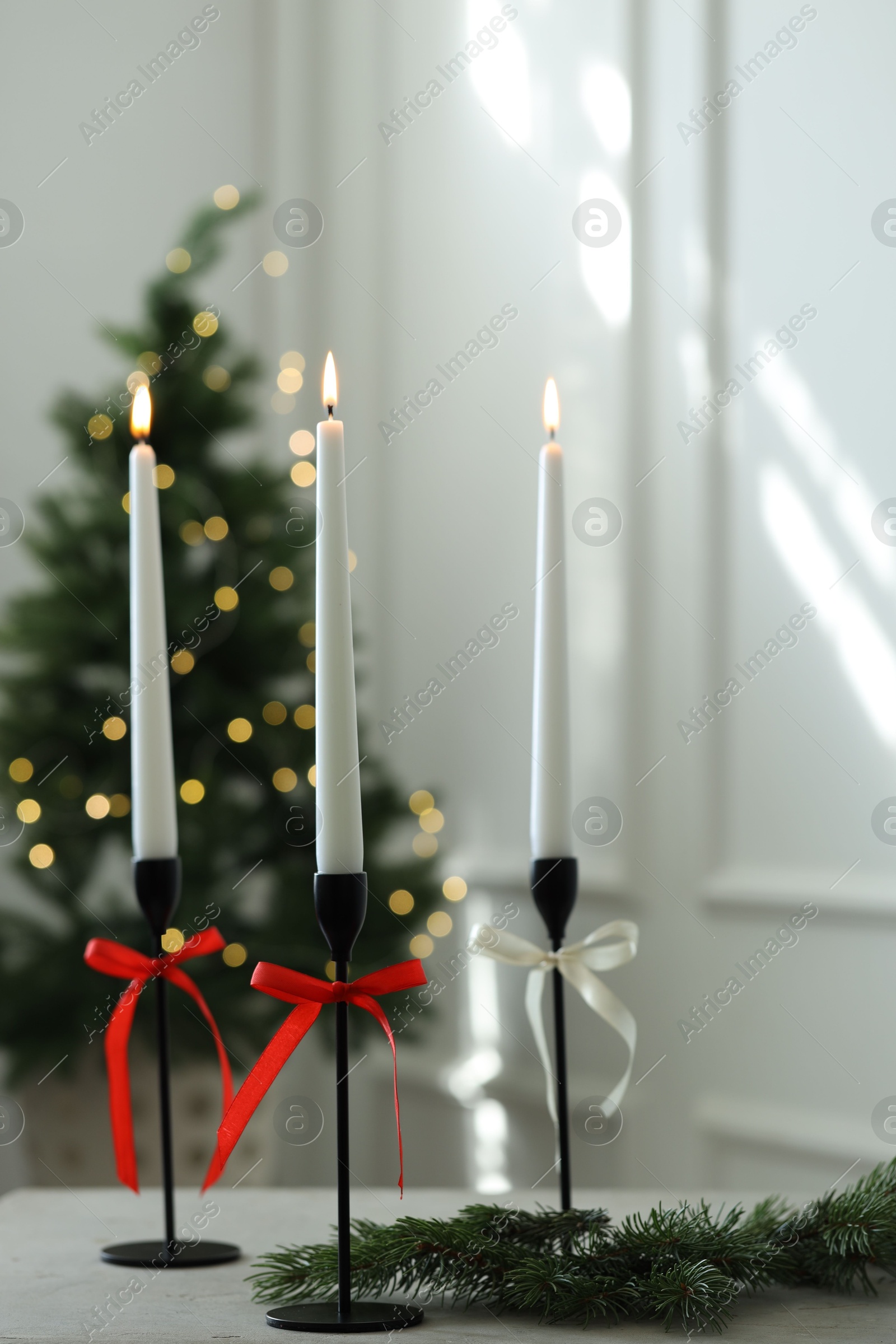 Photo of Burning candles on white table and Christmas tree at home