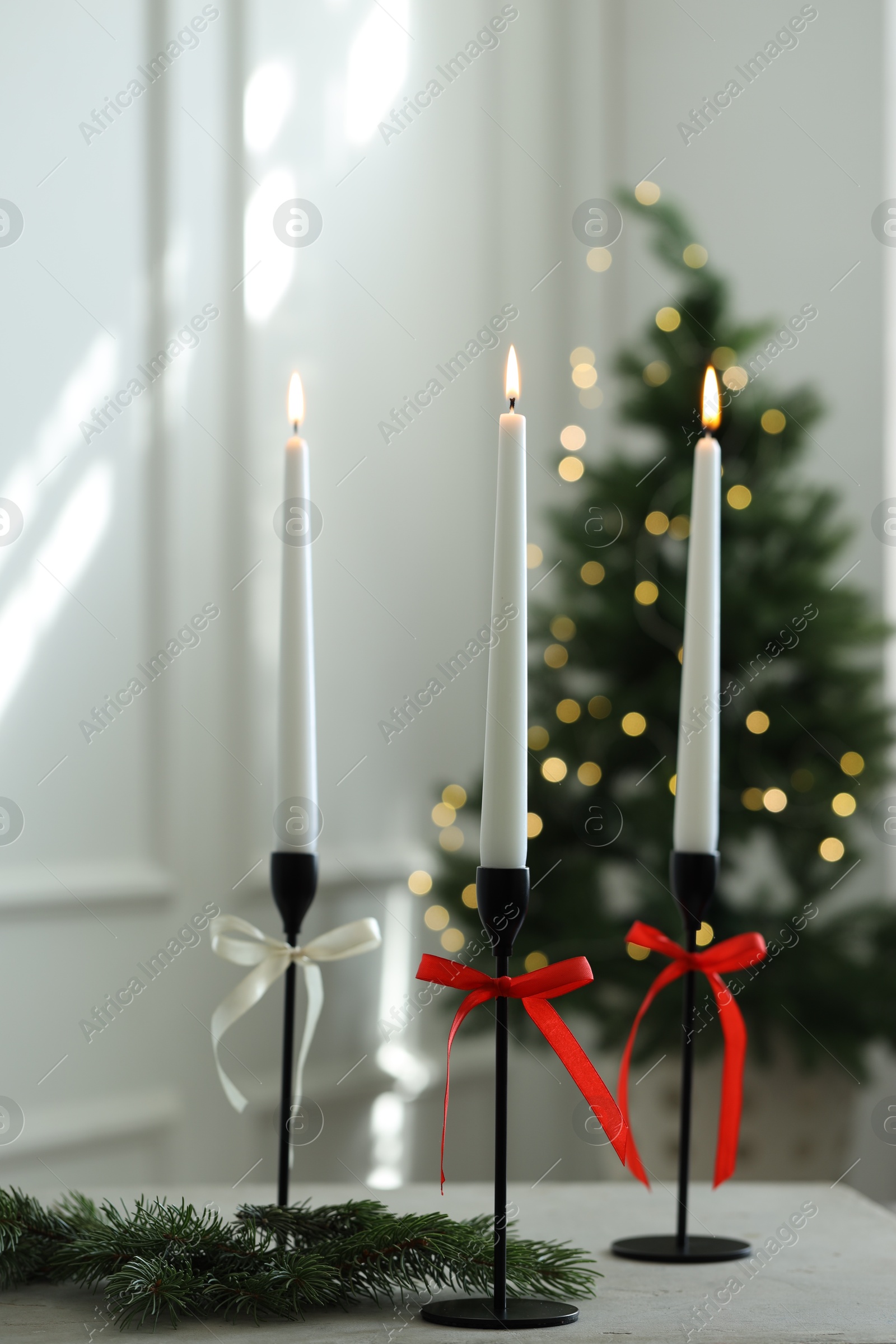 Photo of Burning candles on white table and Christmas tree at home