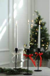 Photo of Burning candles on white table and Christmas tree at home