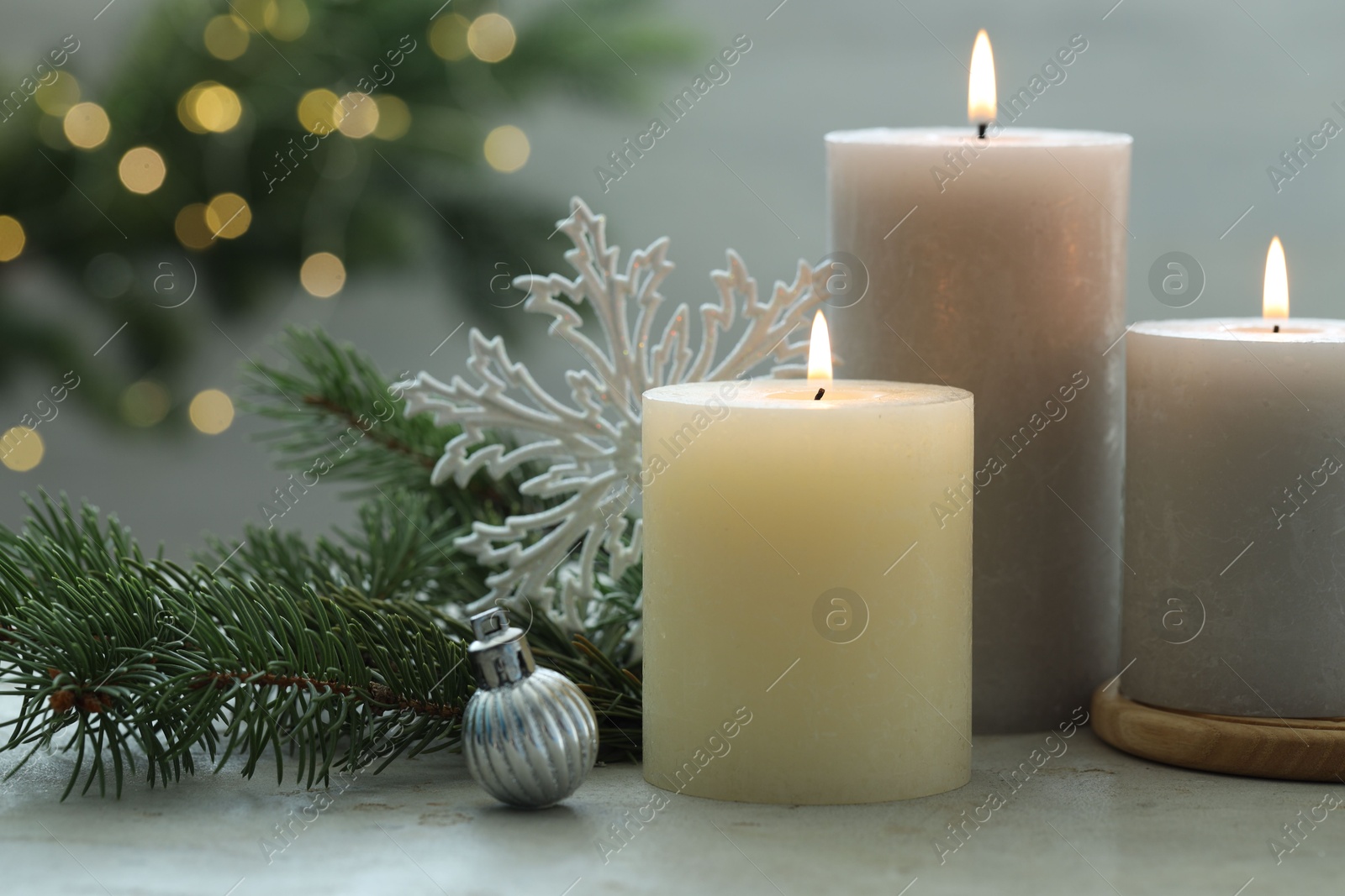 Photo of Burning candles, baubles and fir tree branches on white textured table, closeup